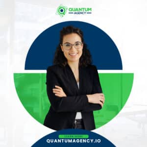 Promotional PR graphic for Quantum Agency showing a smiling businesswoman with glasses and curly hair standing with arms crossed. The central image is isolated inside a split blue and green circle against a faint office background. Includes the Quantum Agency logo and a website link for quantumagency.io at the bottom.